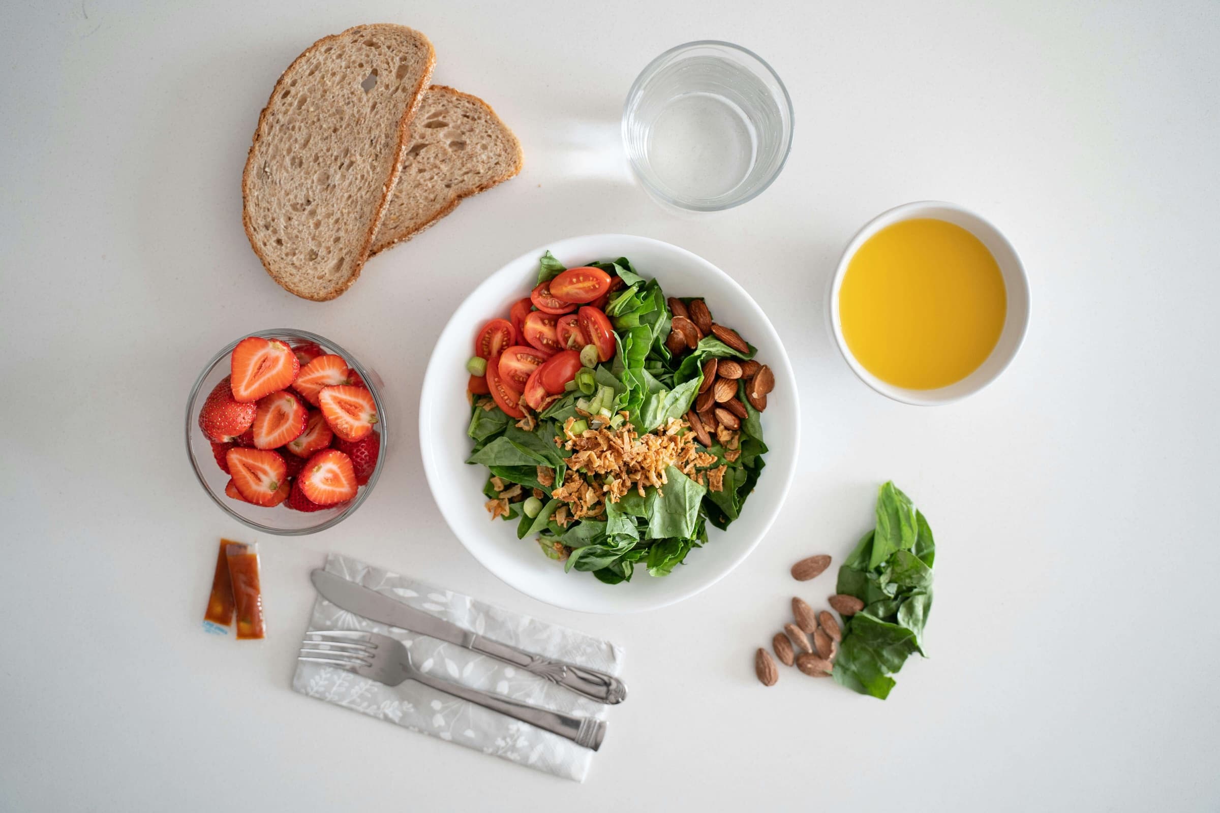 Salad bowl with strawberries, bread and almonds on a white table