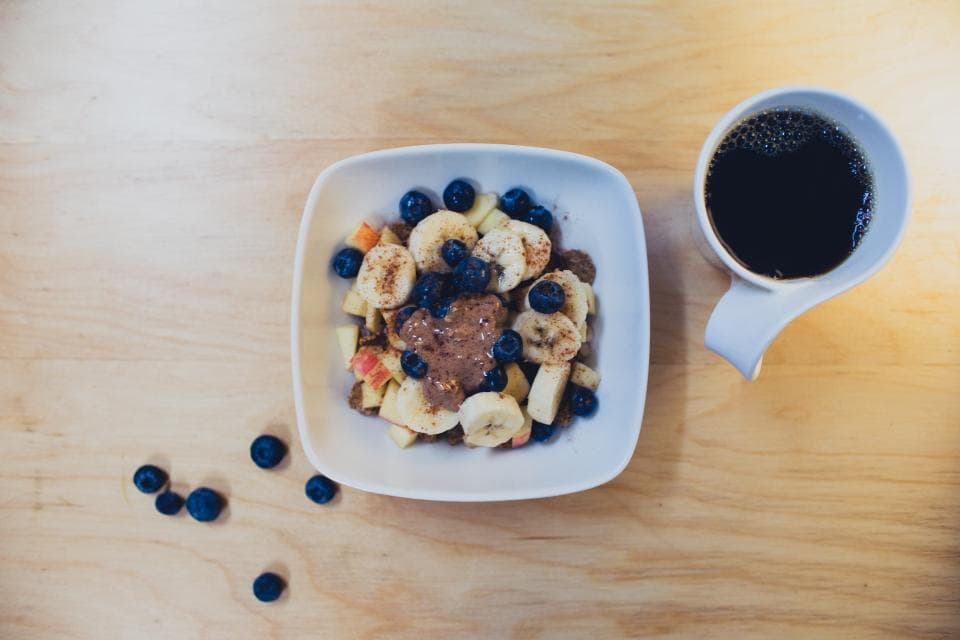 Bowl of oats with banana and blueberries next to a cup of coffee